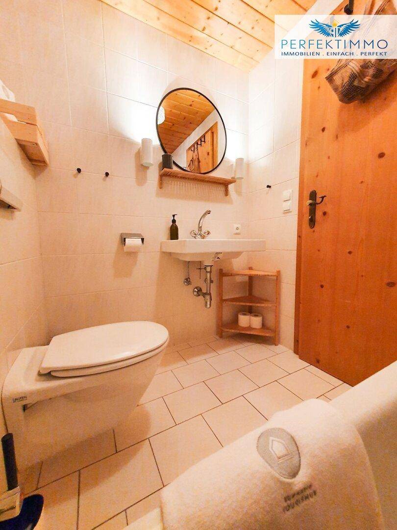 Modernes WC mit weißen Fliesen, Holzdecke und kleinem Waschbecken.