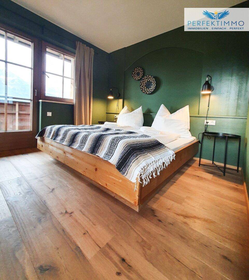 Gemütliches Schlafzimmer mit Holzbett, grüner Wand und Zugang zu einem Balkon.