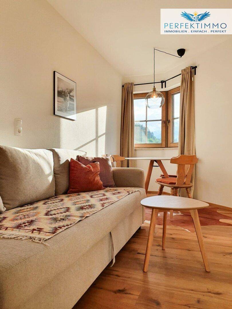 Heller Wohnbereich mit Sofa, Esstisch und Fenstern, die viel Sonnenlicht hereinlassen.