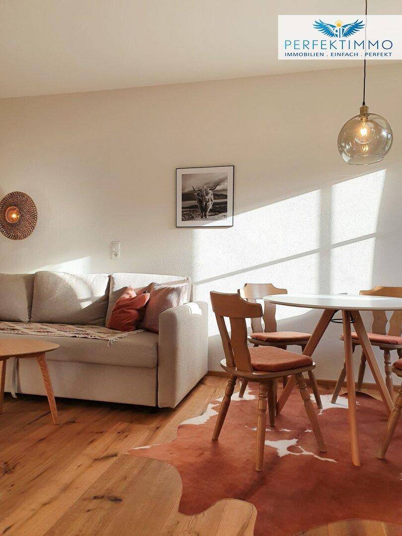 Sonnenverwöhnter Wohn- und Essbereich mit beigem Sofa, Holztisch und Kuhfellteppich.