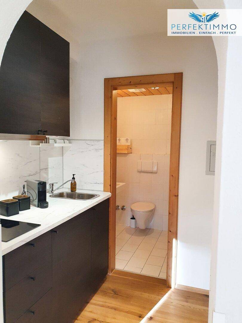 Küchenzeile mit Kochfeld und Spüle, daneben der Eingang zu einem kleinen WC.