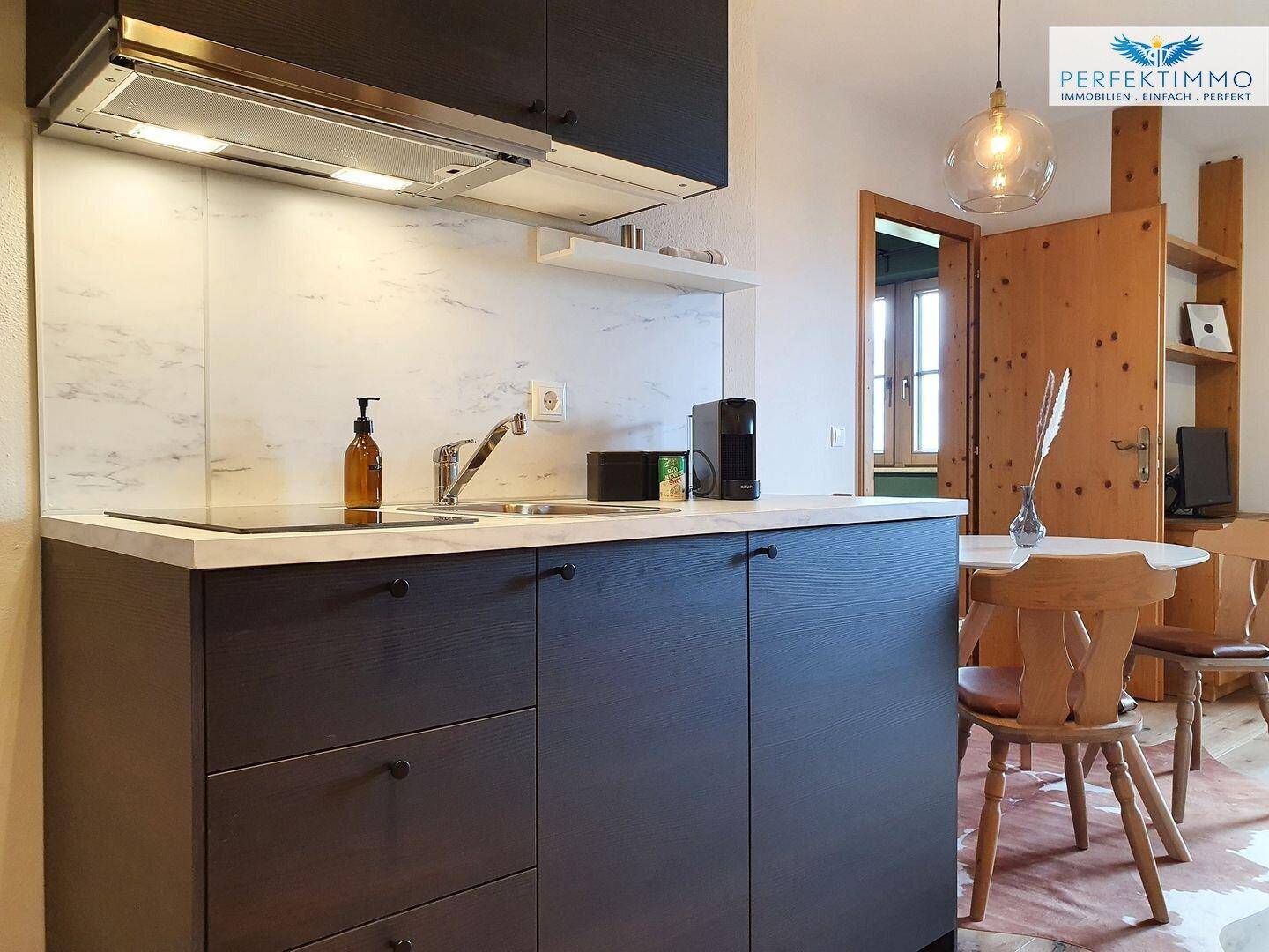 Moderne Küchenzeile mit dunklen Schränken und Essbereich mit Holztisch.