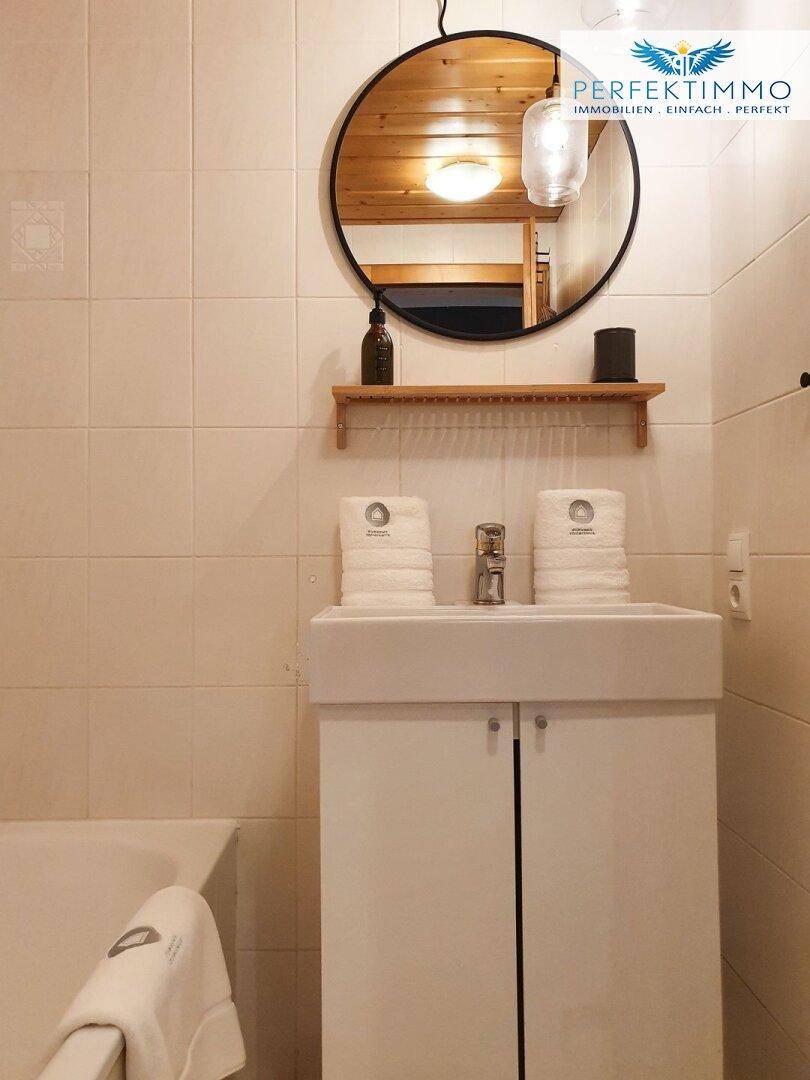 Badezimmer mit modernem Waschbecken, rundem Spiegel und hellen Fliesen.