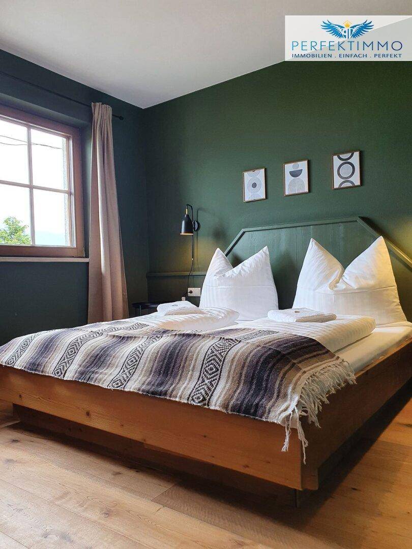 Schlafzimmer mit Holzbett, grüner Akzentwand und minimalistischer Dekoration.