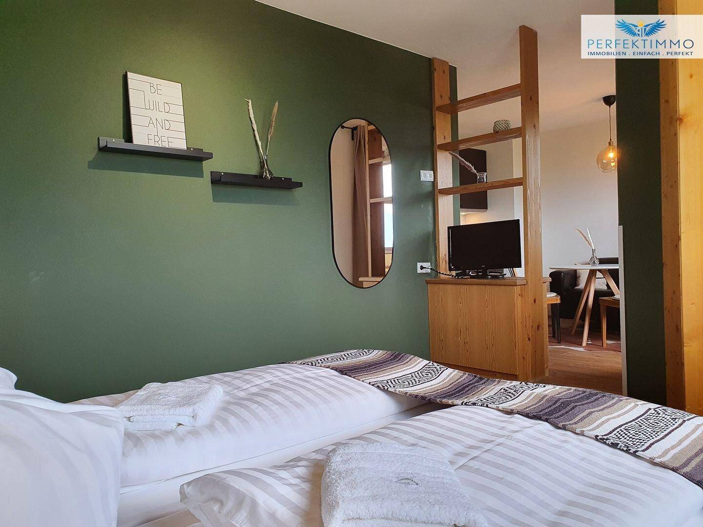 Schlafzimmer mit Holzbett und Regal, offen zum angrenzenden Wohnbereich.