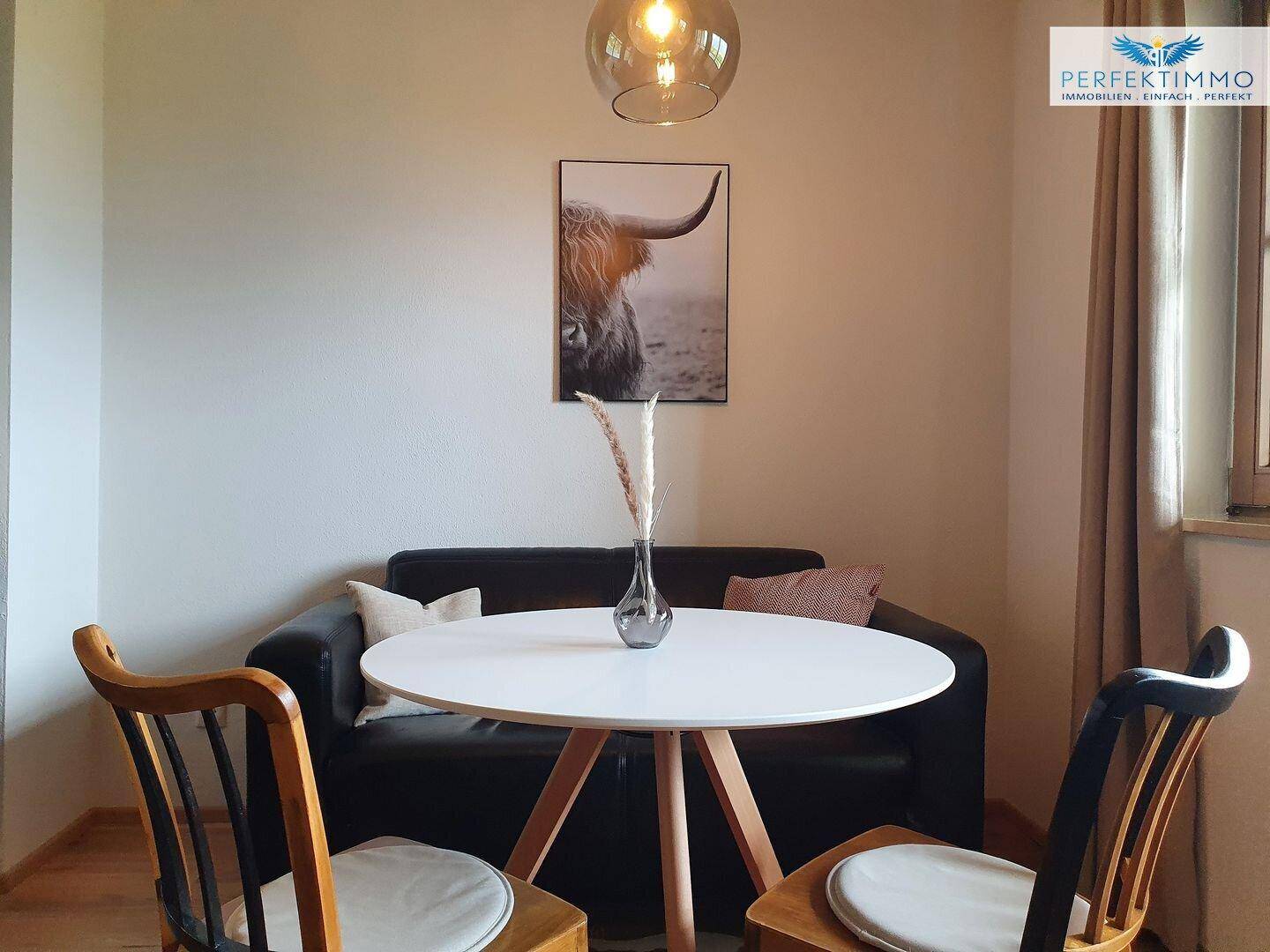 Essbereich mit weißem Tisch und schwarzem Sofa, dekoriert mit einem Kuhfellbild.