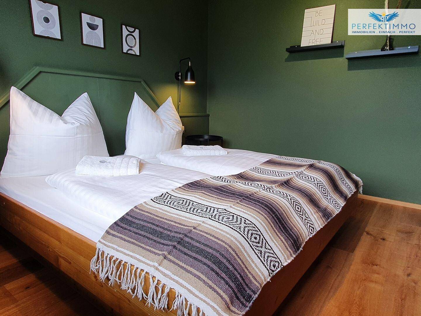 Gemütliches Schlafzimmer mit Holzbett, grüner Wand und dekorativen Elementen.