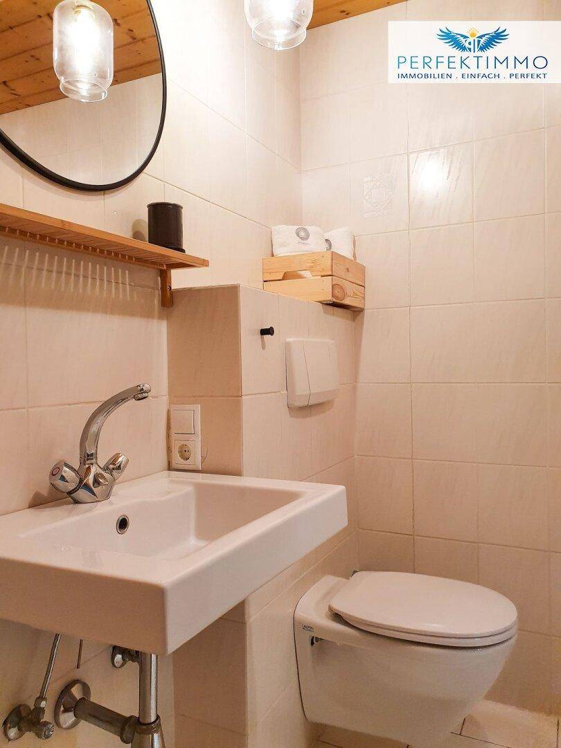 Modernes WC mit weißem Waschbecken, Wand-WC und hellen Fliesen.