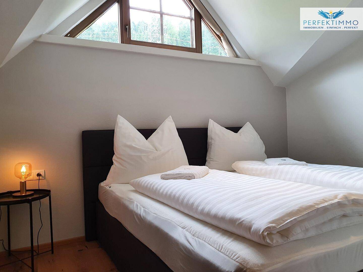 Gemütliches Schlafzimmer mit Dachschräge, Doppelbett und einem Fenster mit Blick ins Grüne.