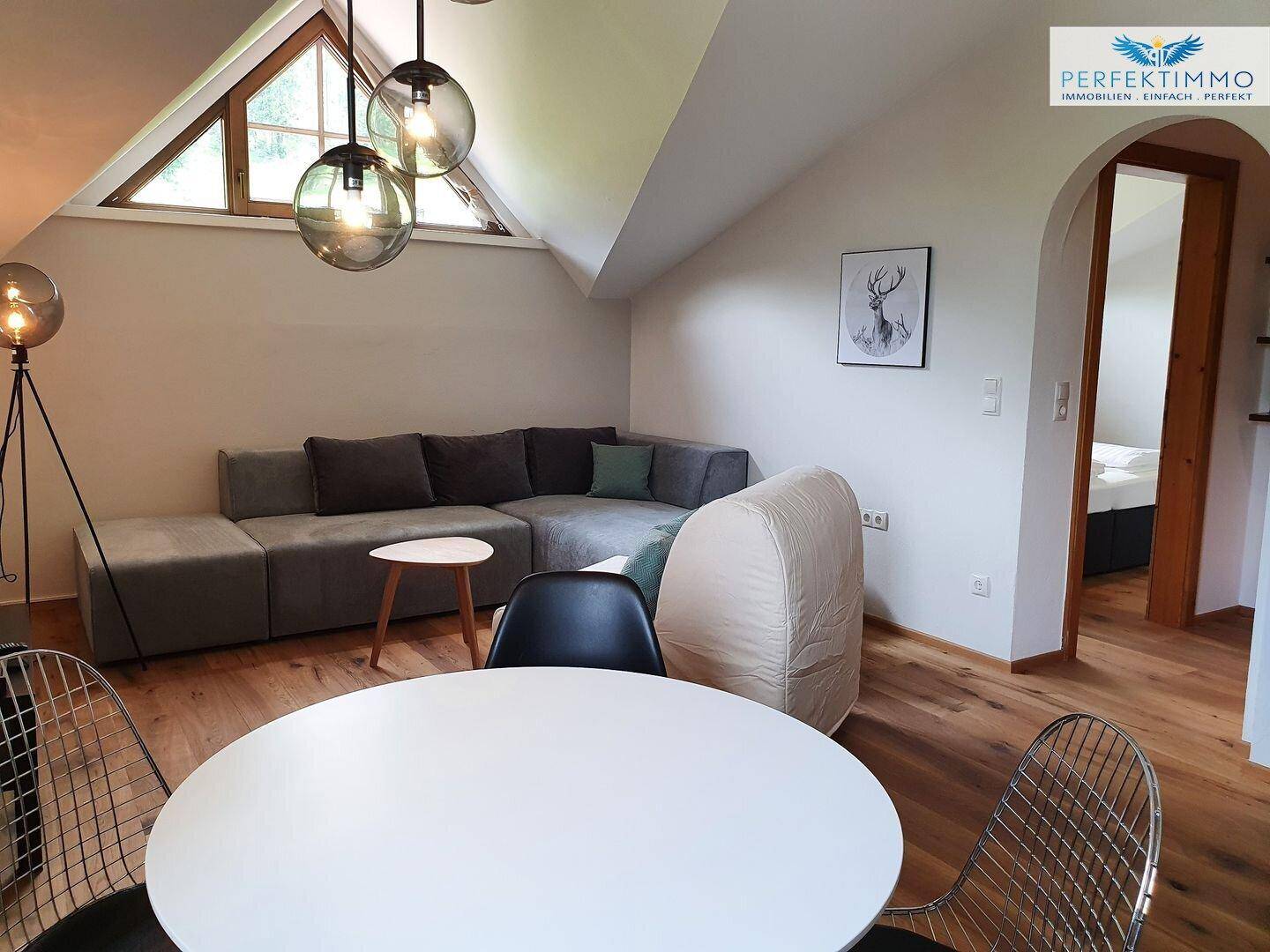 Heller Wohnbereich mit Ecksofa, Esstisch und Zugang zu einem Schlafzimmer unter der Dachschräge.