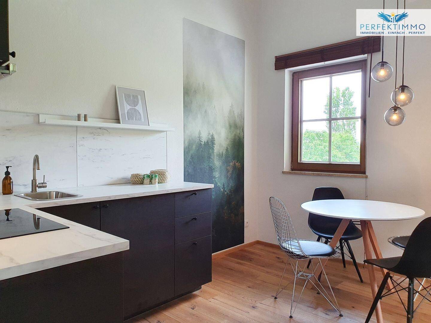 Moderne Küchenzeile mit dunklen Schränken, heller Arbeitsplatte und Essbereich am Fenster.