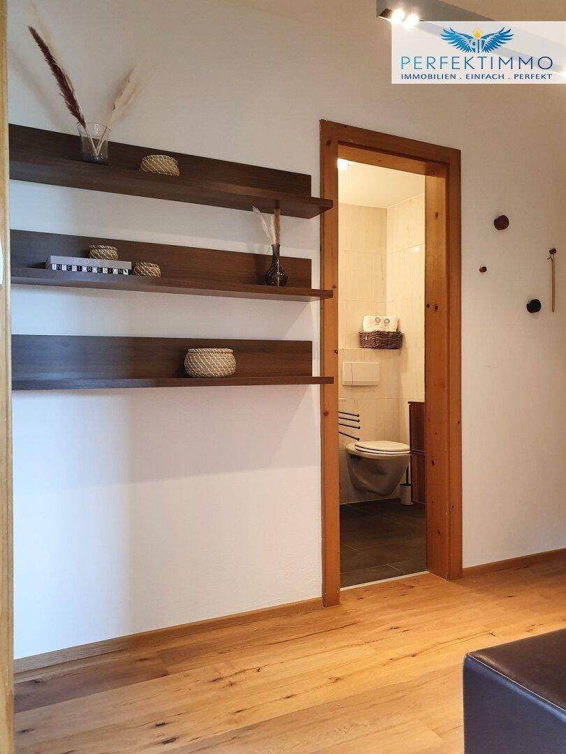Flur mit Holzregalen und Blick in ein hell gefliestes Badezimmer mit WC.