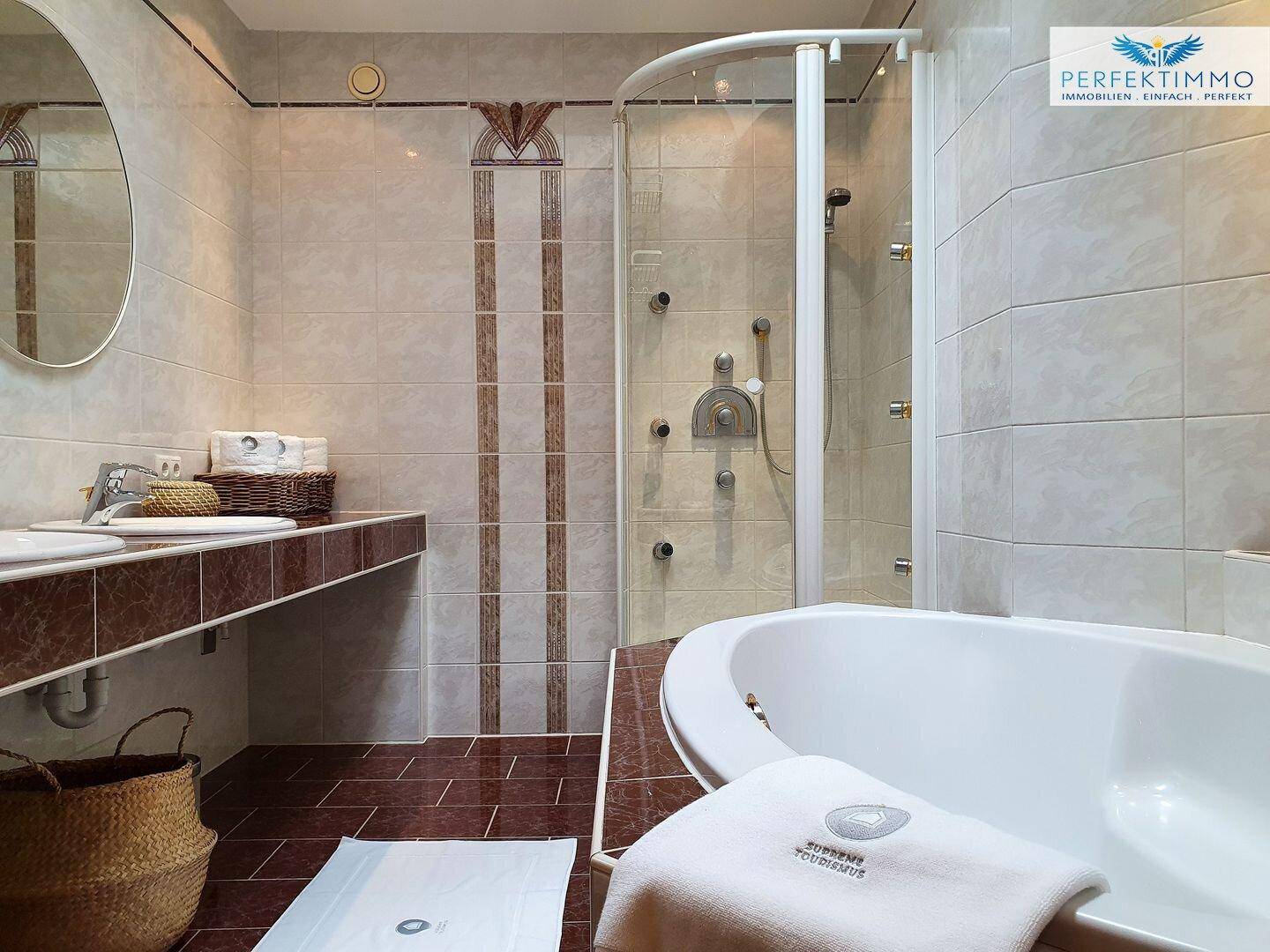 Geräumiges Badezimmer mit Badewanne, Duschkabine und Doppelwaschbecken in warmen Farbtönen.
