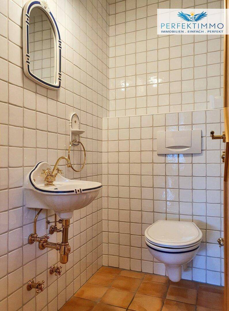 Kleines Gäste-WC mit nostalgischem Waschbecken, Toilette und Terrakotta-Fliesenboden.