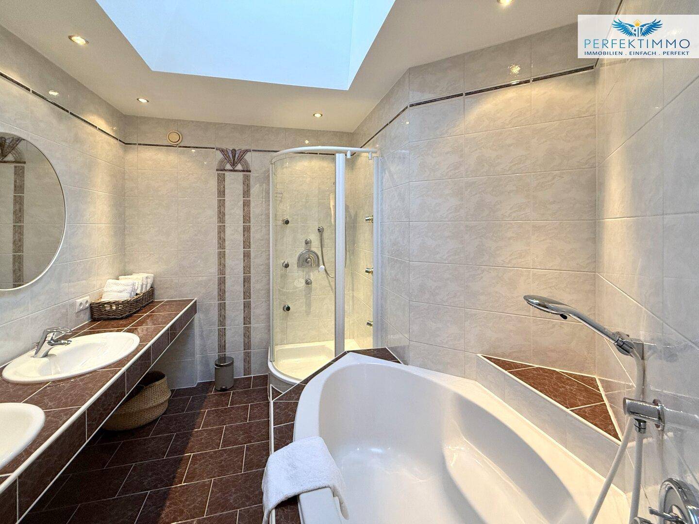 Helles Badezimmer mit Eckbadewanne, Duschkabine, Doppelwaschbecken und Oberlicht.