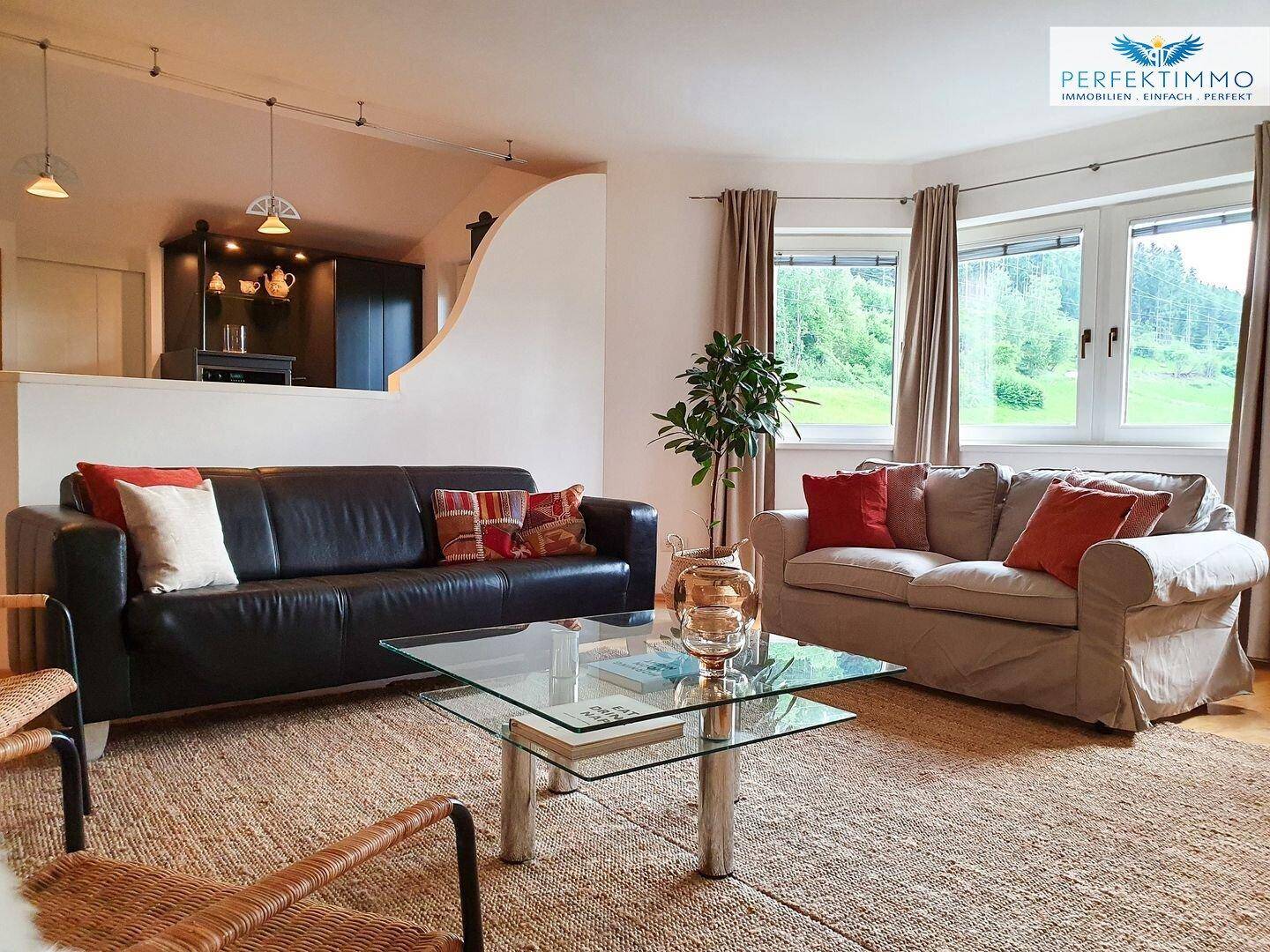 Gemütliches Wohnzimmer mit zwei Sofas, Glastisch und Blick ins Grüne durch große Fenster.
