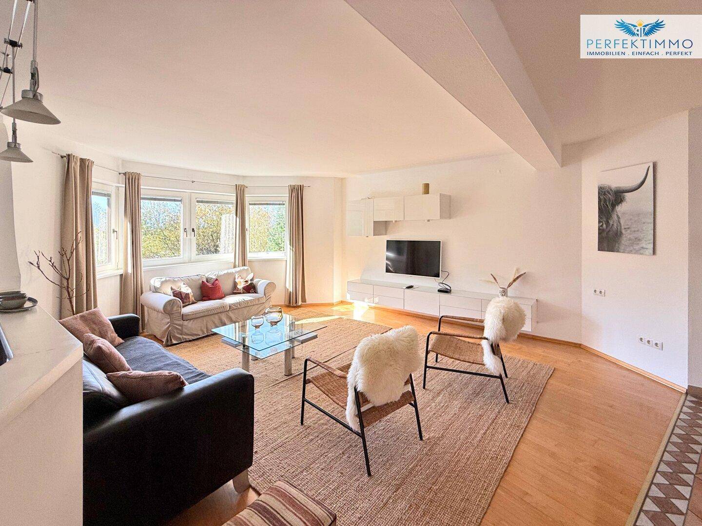 Geräumiges Wohnzimmer mit Sofas, TV-Möbeln und großen Fenstern mit Blick ins Grüne.