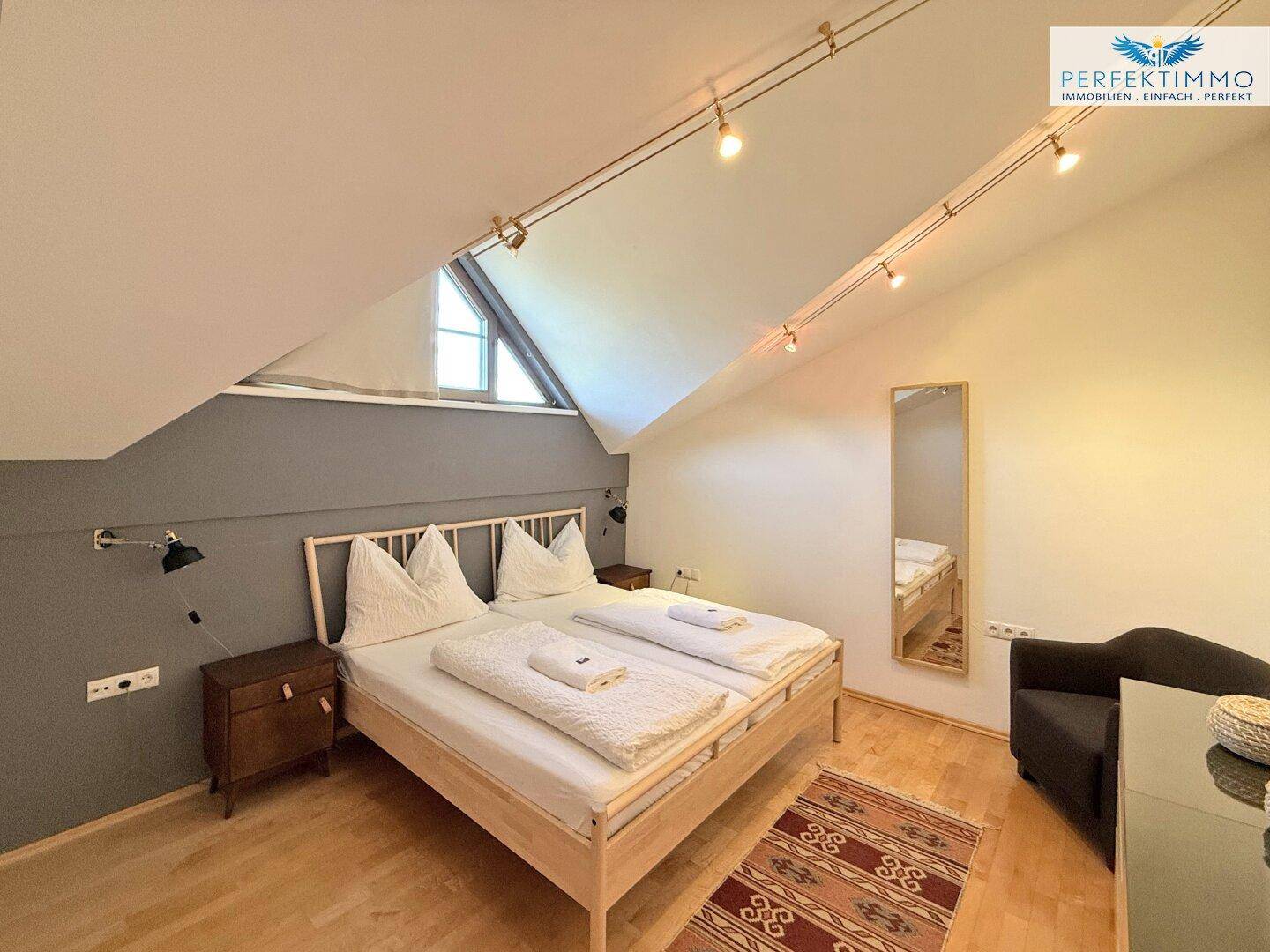 Geräumiges Schlafzimmer im Dachgeschoss mit Holzboden, Dachschräge und großem Bett.