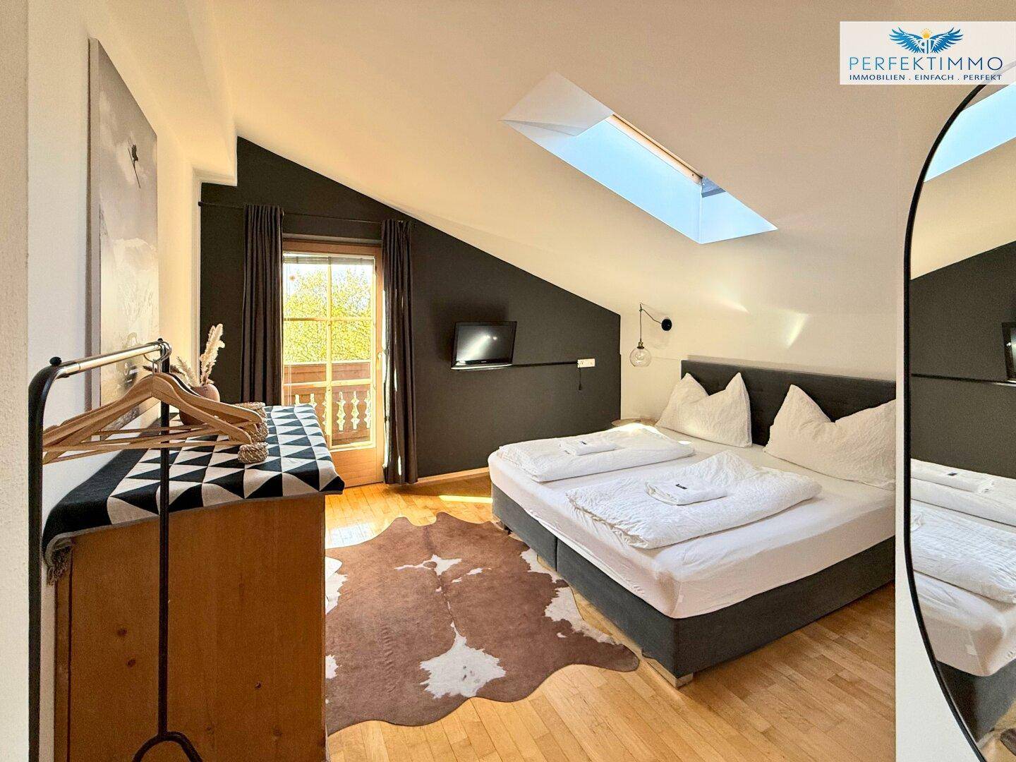 Schlafzimmer mit Doppelbett, Holzboden, Dachschräge, Oberlicht und Zugang zum Balkon.
