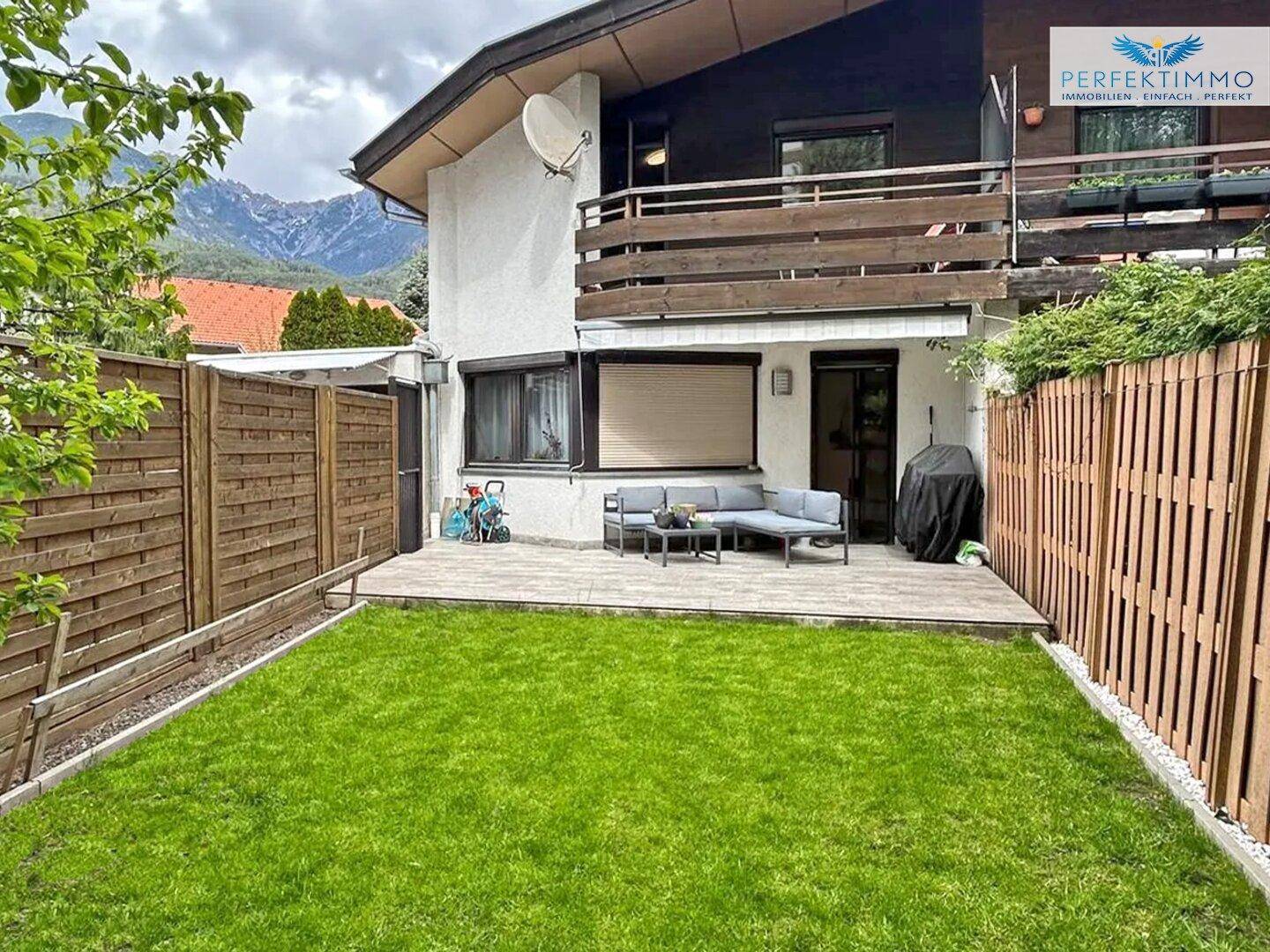 Außenbereich mit Terrasse, gepflegtem Rasen und beeindruckendem Bergblick im Hintergrund.