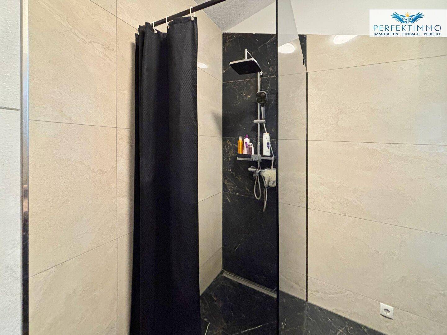 Duschbereich im Badezimmer mit modernen Fliesen in Beige und Schwarz, ausgestattet mit einer Regendusche.