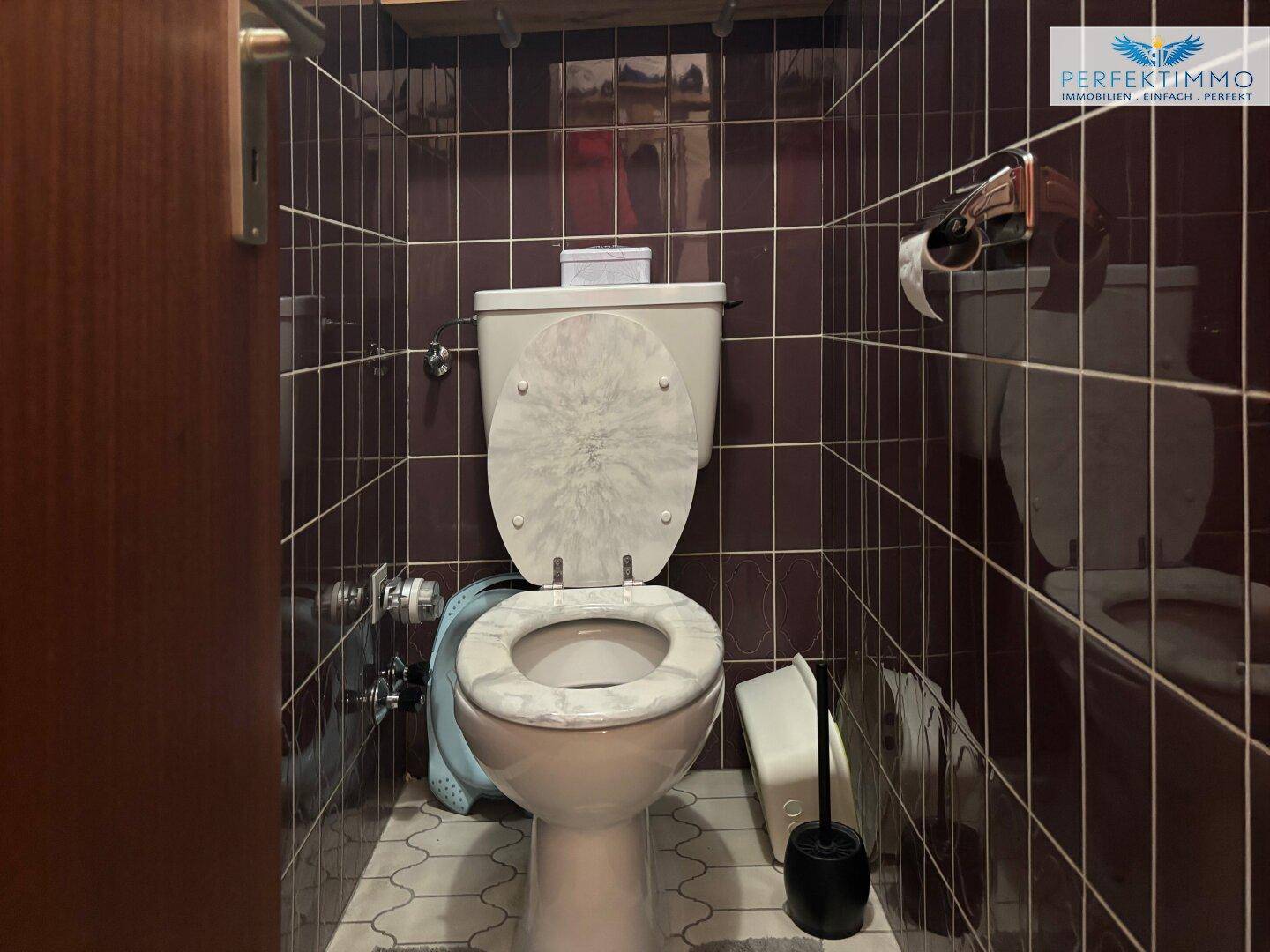 Separates WC mit braunen Fliesen und Standard-Toilette, sauber und funktional.