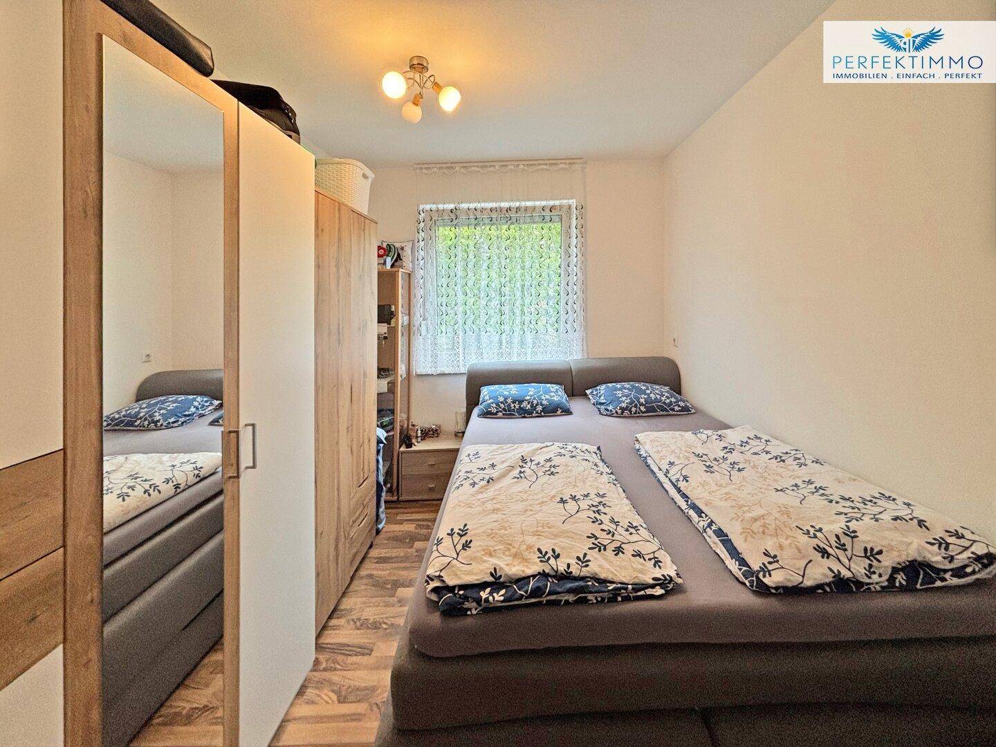 Schlafzimmer mit Doppelbett, großem Spiegelschrank und Fenster, hell und funktional eingerichtet.