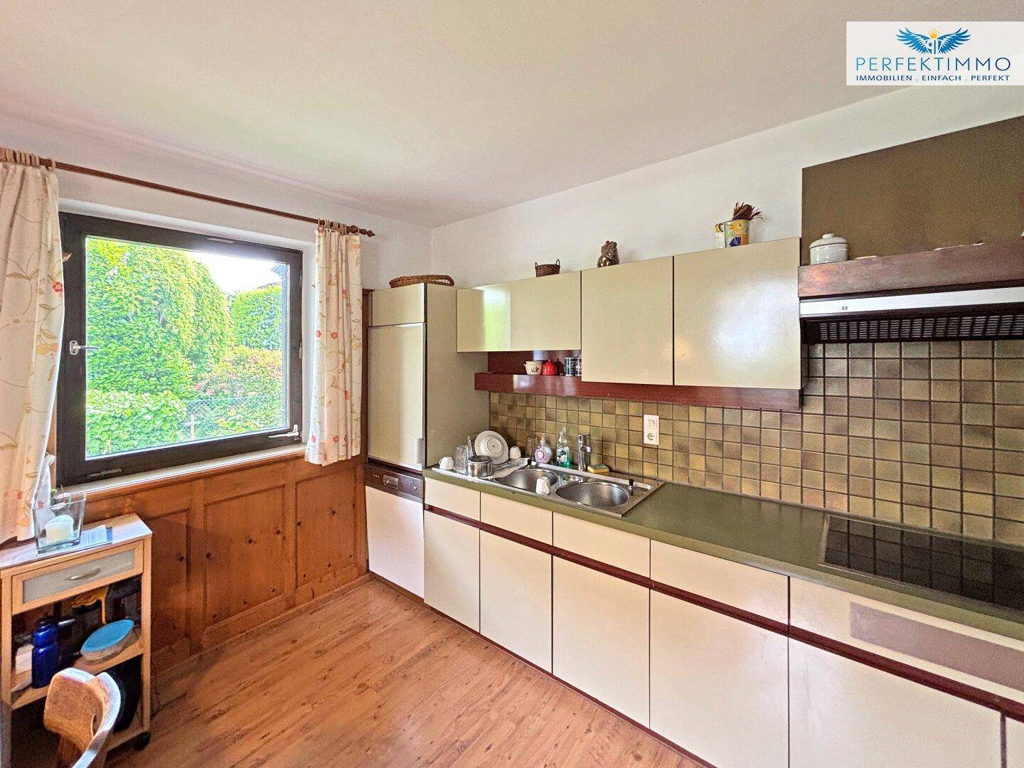 Funktionale Küche mit hellen Schränken, Fliesenrückwand und einem Fenster mit Blick in den Garten.