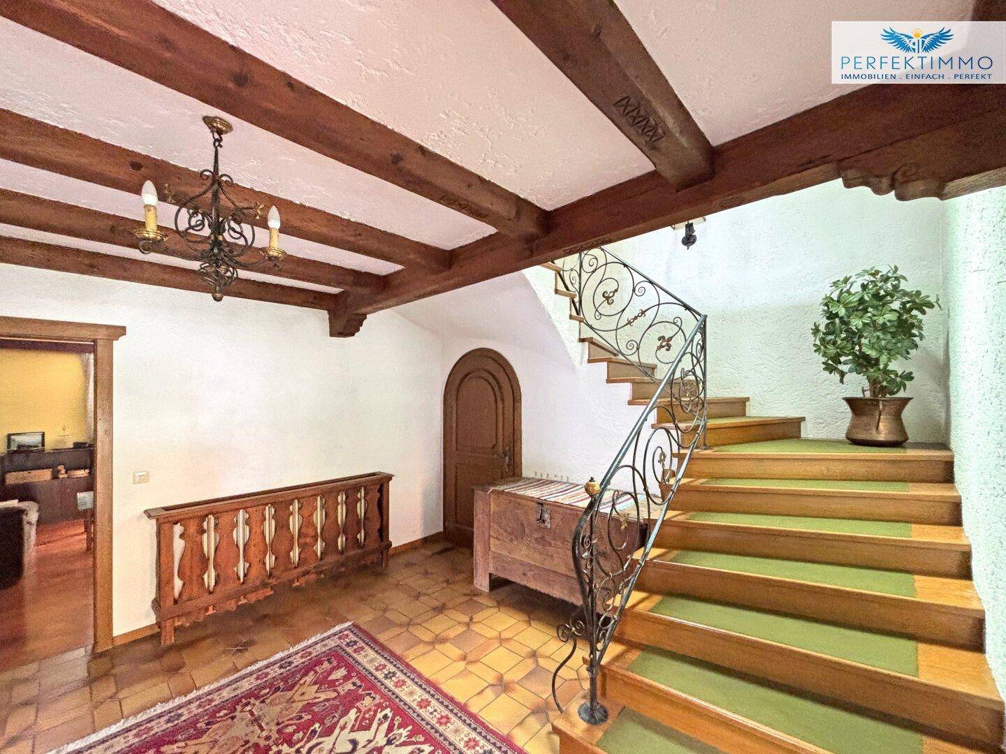 Geräumiger Flur mit einer geschwungenen Treppe, Fliesenboden und Holzbalken an der Decke.