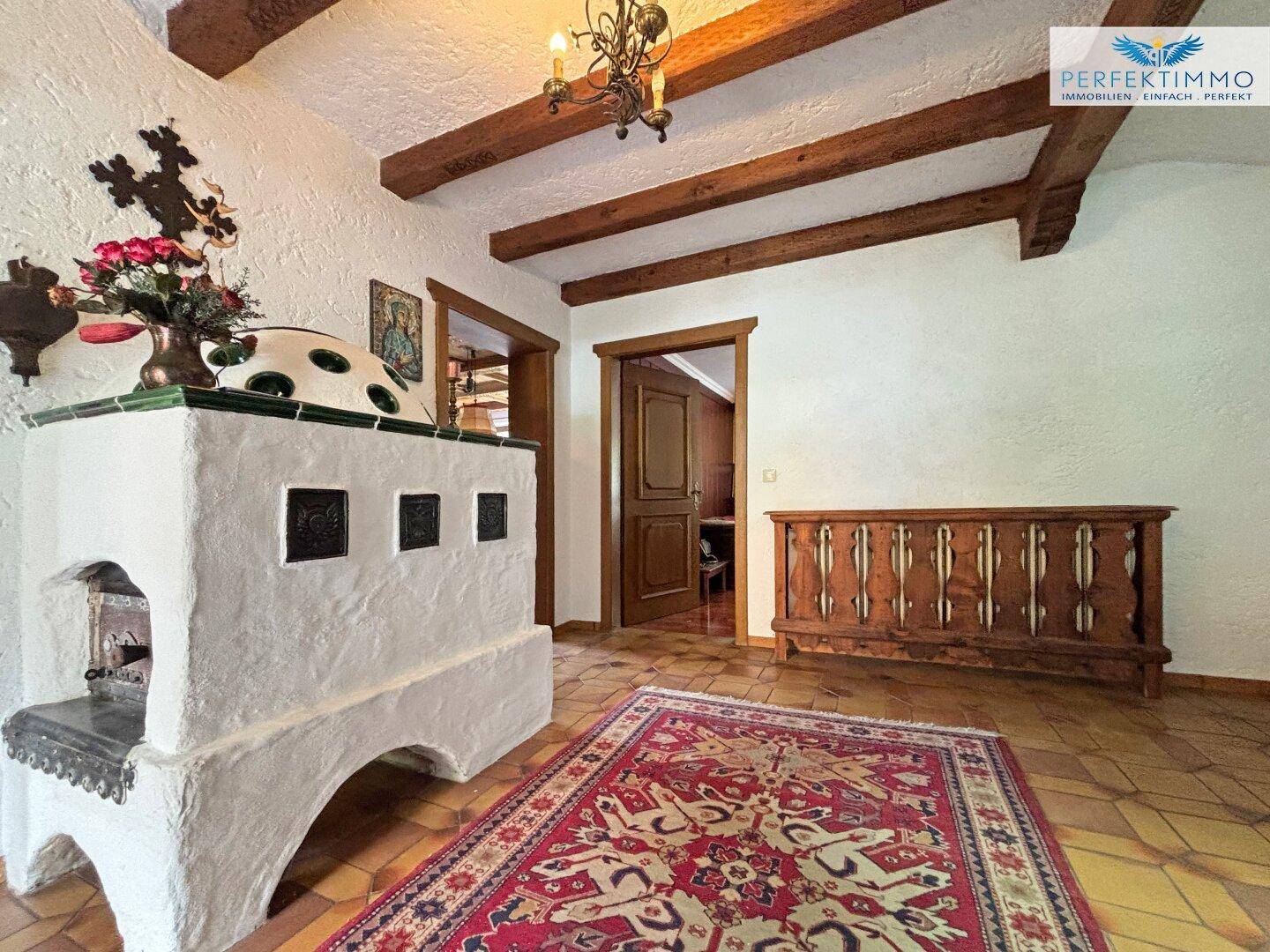 Traditioneller Eingangsbereich mit einem Kachelofen, Fliesenboden und Holzbalken an der Decke.