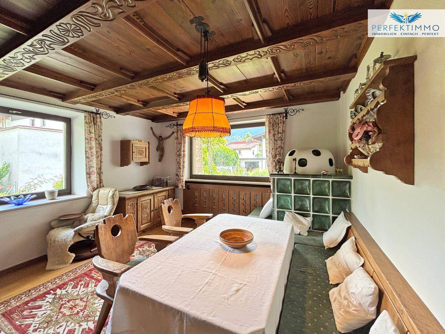 Gemütlicher Essbereich mit Holztisch, Eckbank und einem traditionellen grünen Kachelofen.