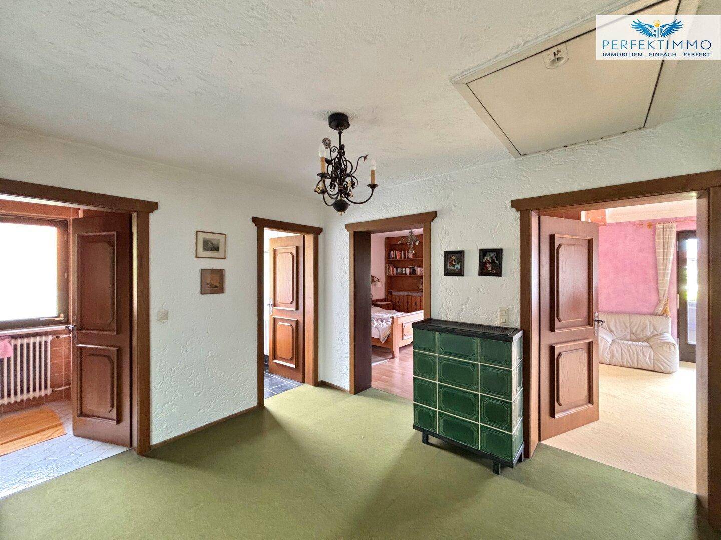 Obergeschoss-Flur mit grünem Teppichboden, mehreren Türen und einem traditionellen Kachelofen.