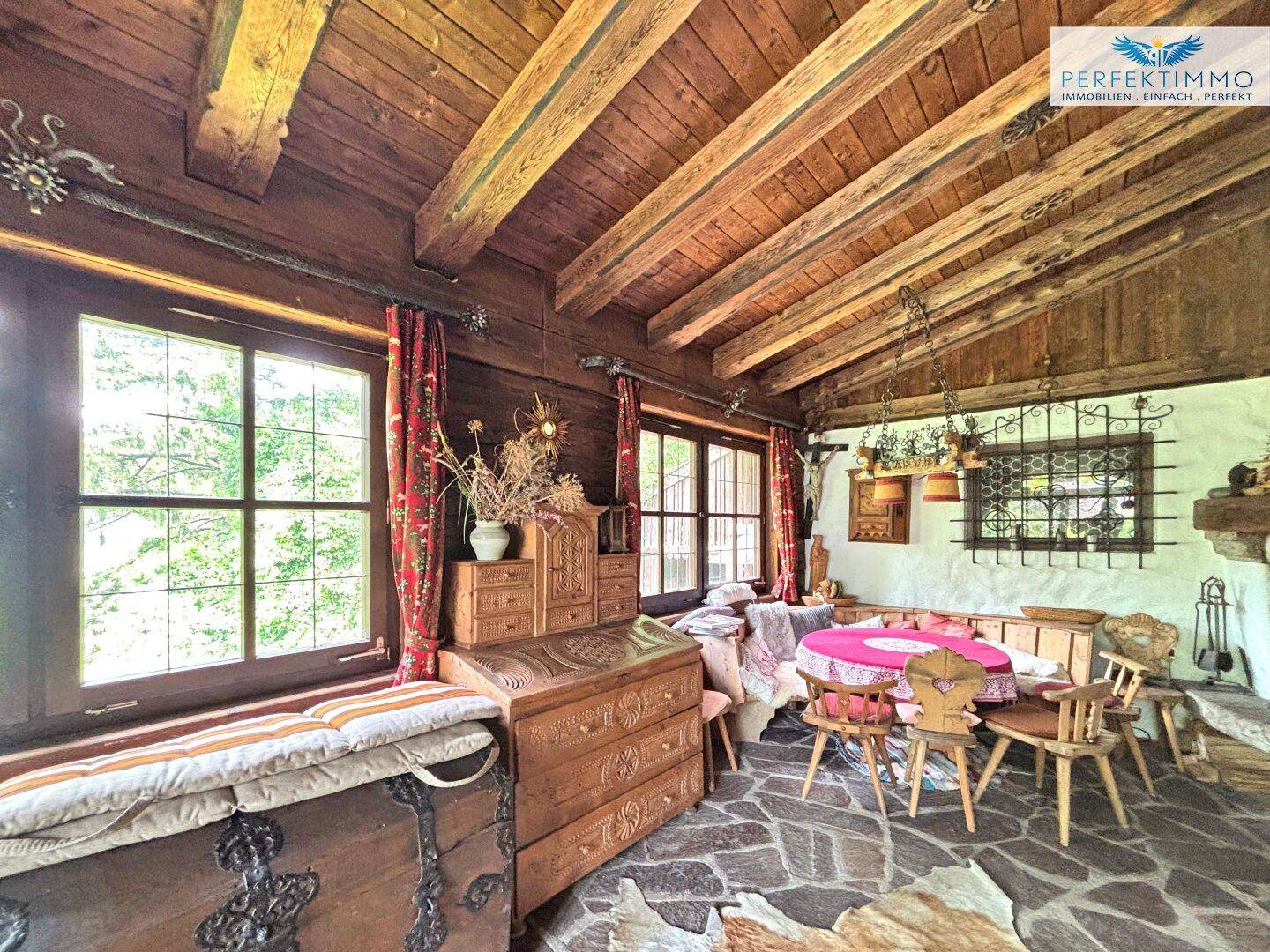 Rustikaler Wohn- und Essbereich mit Holzbalkendecke, Steinboden und traditionellen Holzmöbeln.