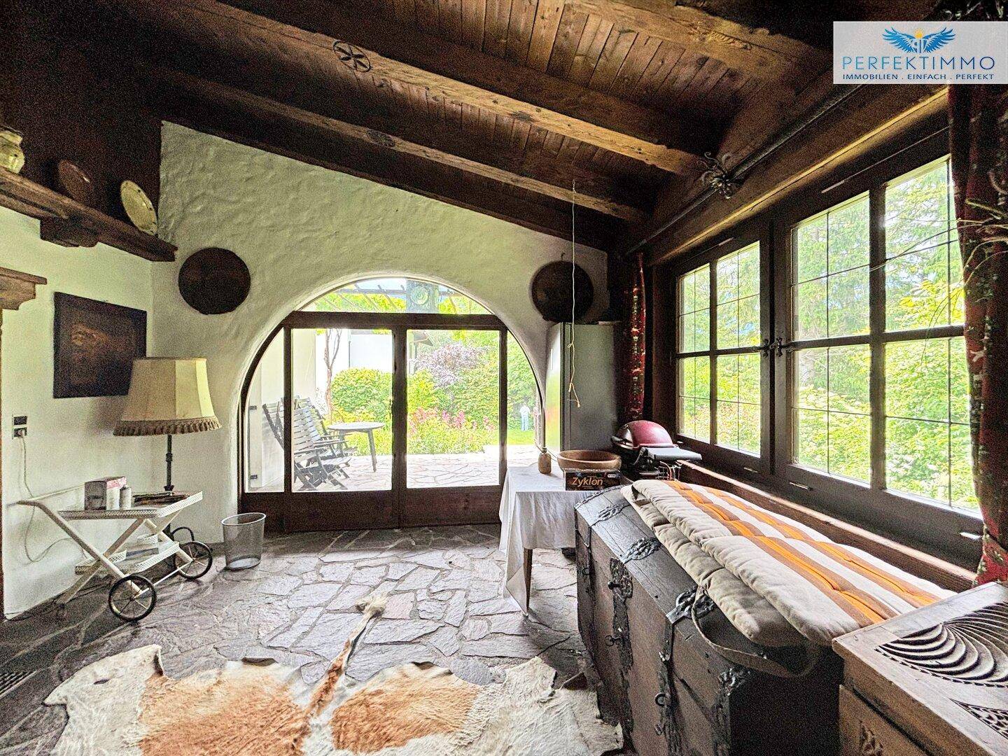 Heller Wohnbereich mit Steinboden, Holzbalkendecke und Zugang zu einer überdachten Terrasse.