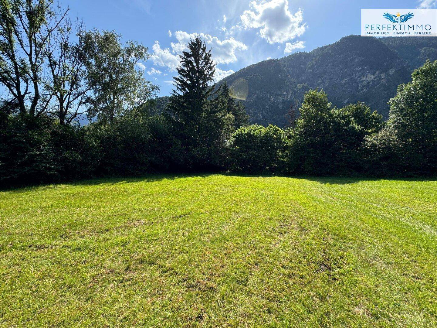 Sonnige Rasenfläche mit weitem Blick auf die Berge und umgebende grüne Landschaft.
