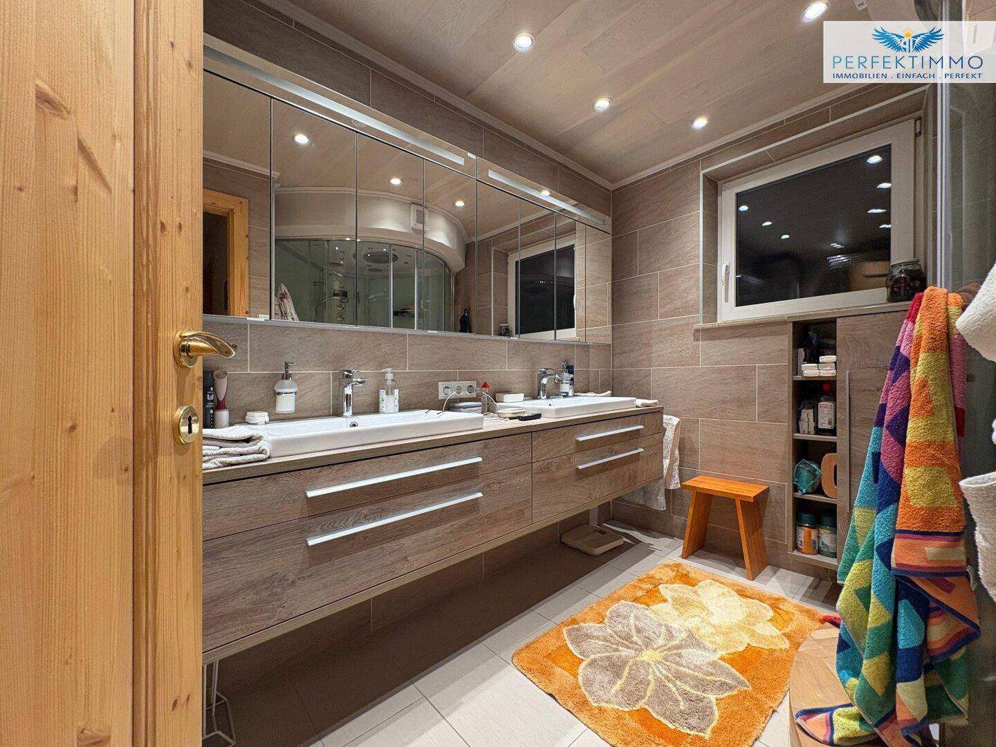 Modernes Badezimmer mit Doppelwaschbecken, großem Spiegelschrank und hellen Fliesen.