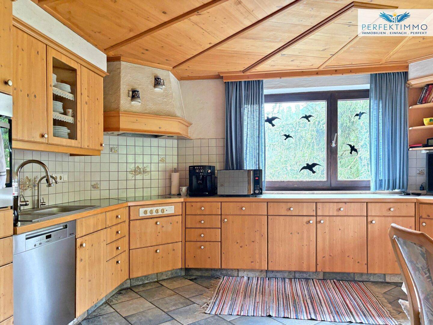 Traditionelle Holzküche mit Fliesenboden, Einbaugeräten und Fenster mit Blick ins Grüne.