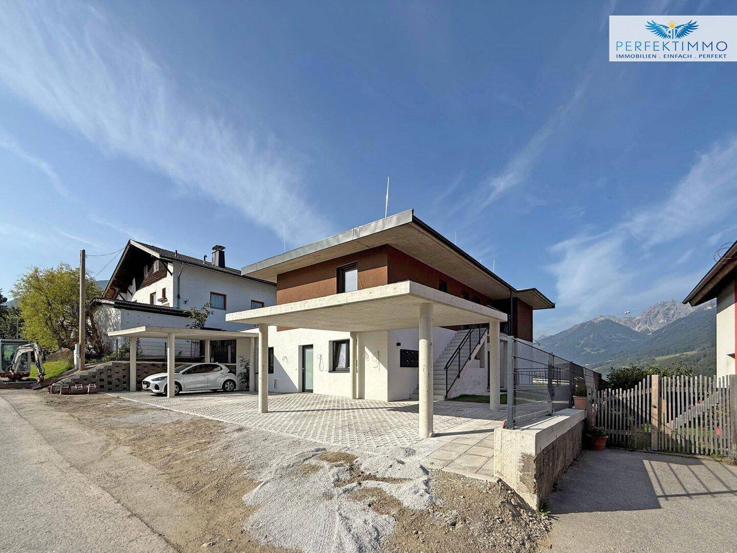 Seitenansicht des modernen Hauses mit Carports und Blick auf die umliegende Berglandschaft.