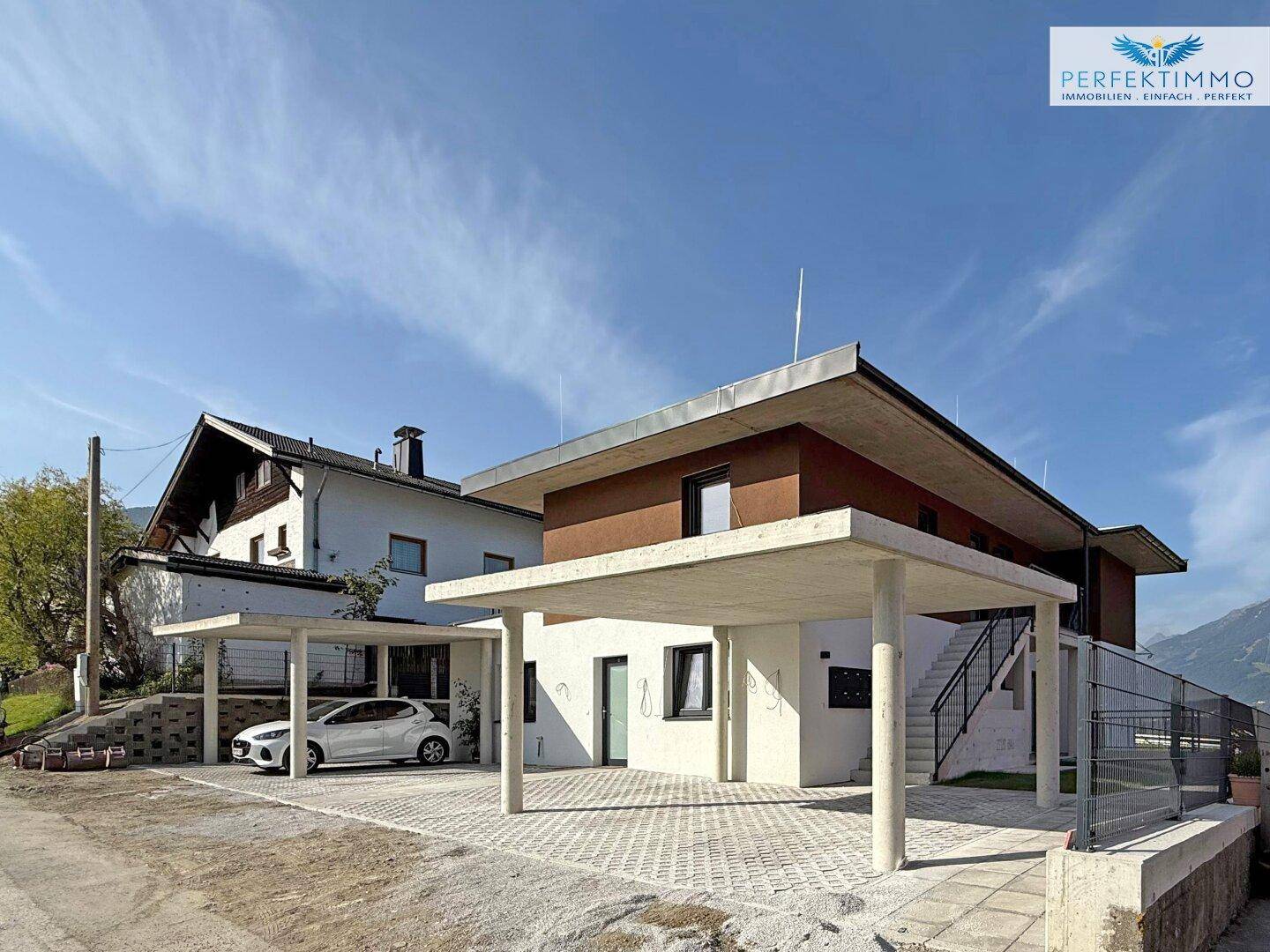 Modernes Haus mit zwei Carports und klarem Himmel. Die Fassade ist in Weiß und Braun gehalten.