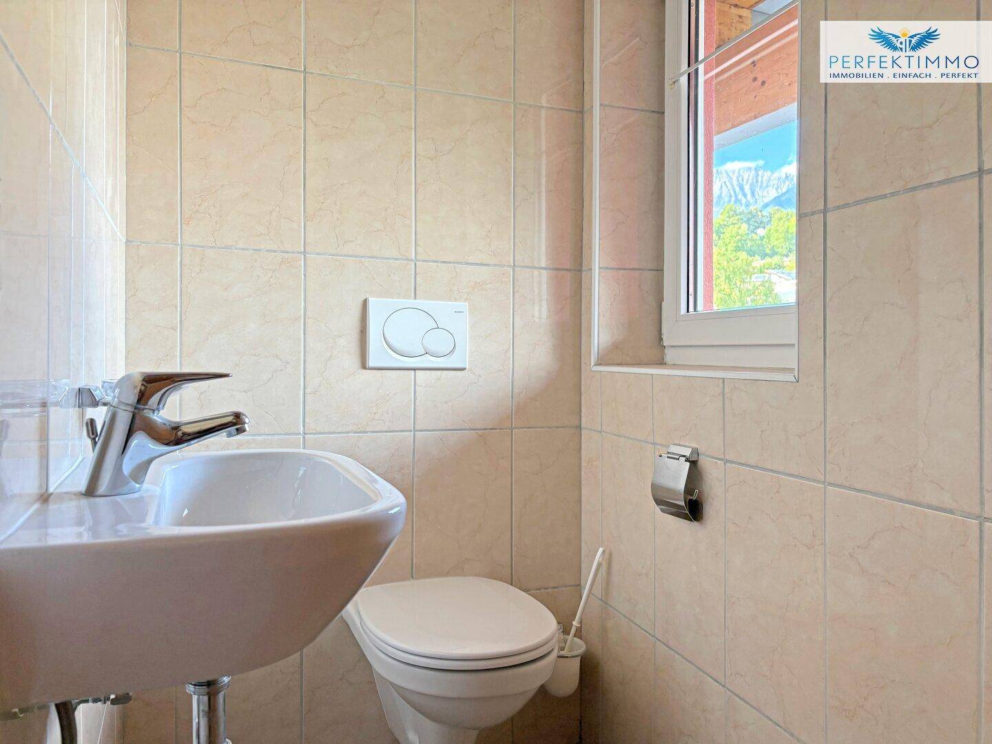 Kleines Gäste-WC mit Fenster, Toilette und Handwaschbecken in hellen beigefarbenen Fliesen.