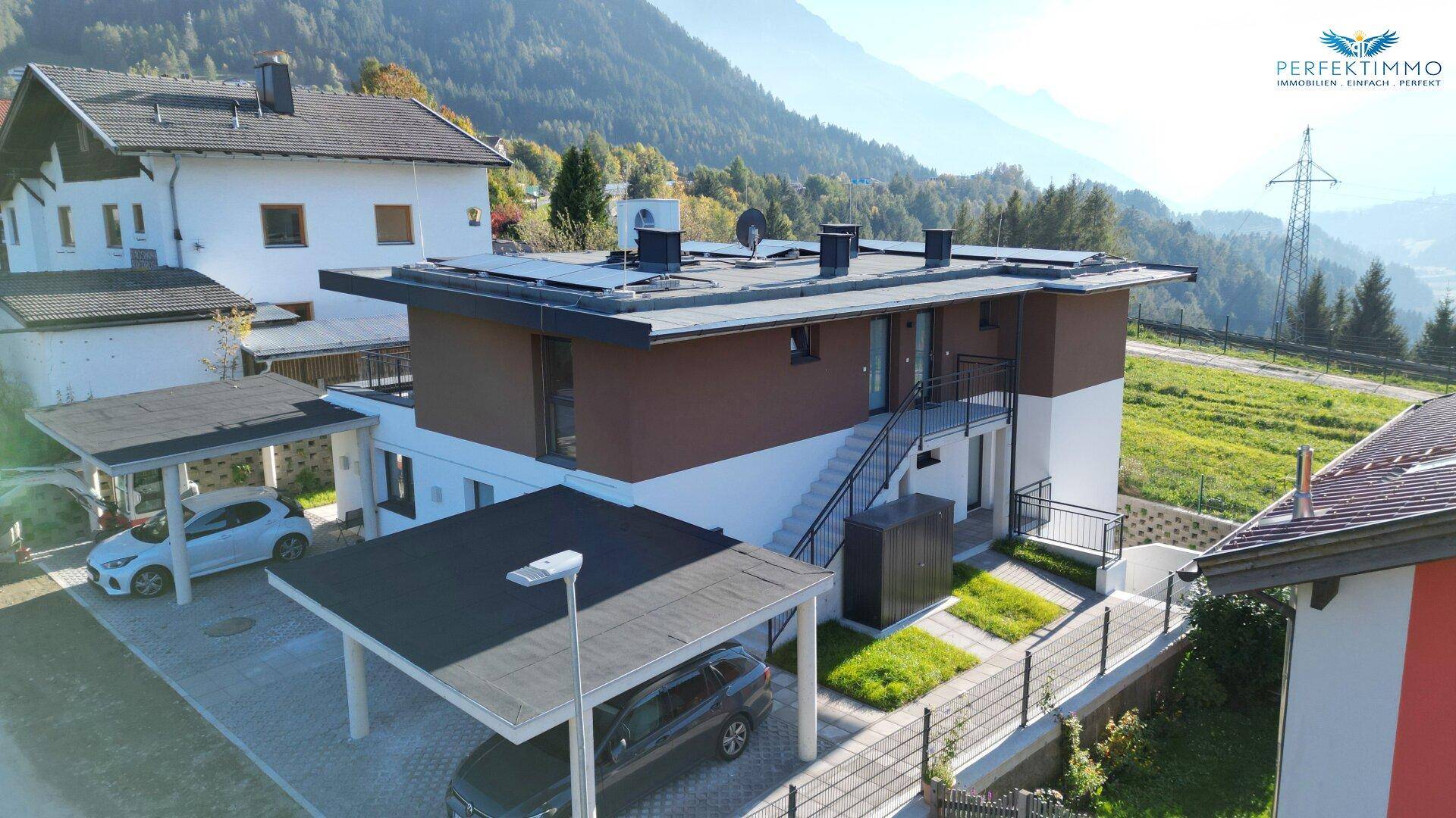 Ansicht eines modernen Wohnhauses mit Solaranlage, Carports und gepflegter Außenanlage.