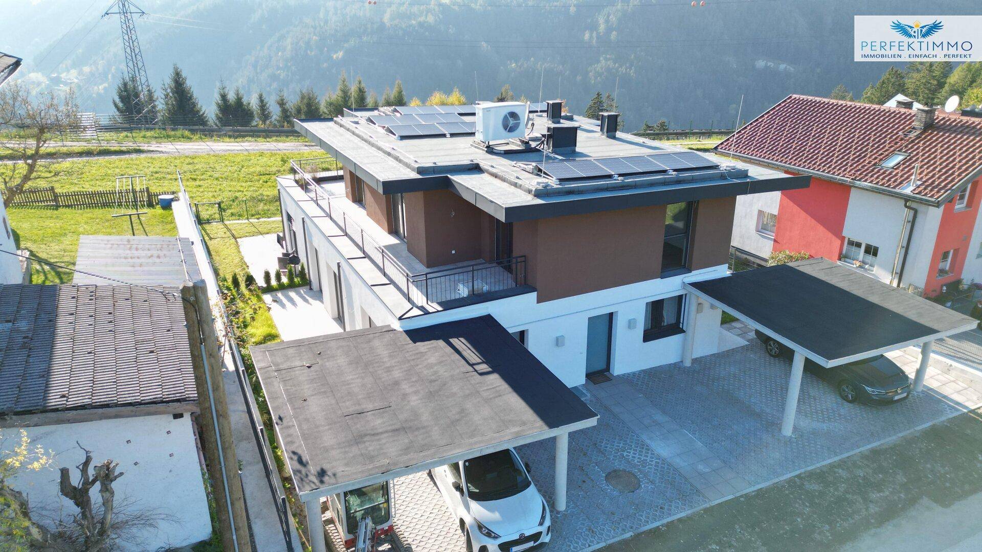 Luftaufnahme eines modernen Wohnhauses mit Solaranlage, Carports und Bergblick.