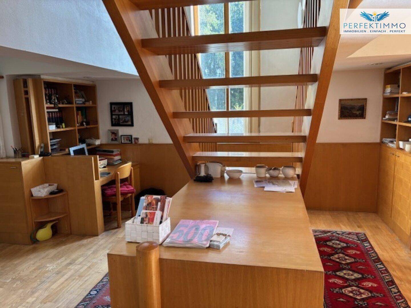 Heller Wohnbereich mit Holztreppe, Schreibtisch und integrierten Holzregalen.