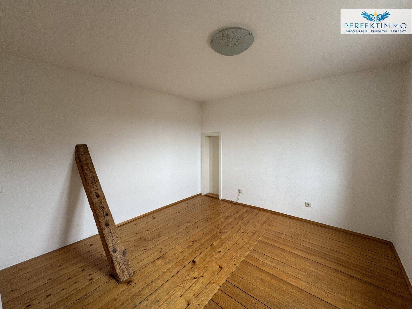 Heller Raum mit Holzdielenboden und einem sichtbaren Holzbalken.