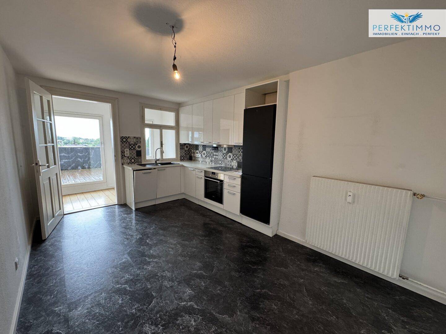 Moderne Einbauküche mit weißen Schränken, dunklem Boden und Zugang zur Terrasse.