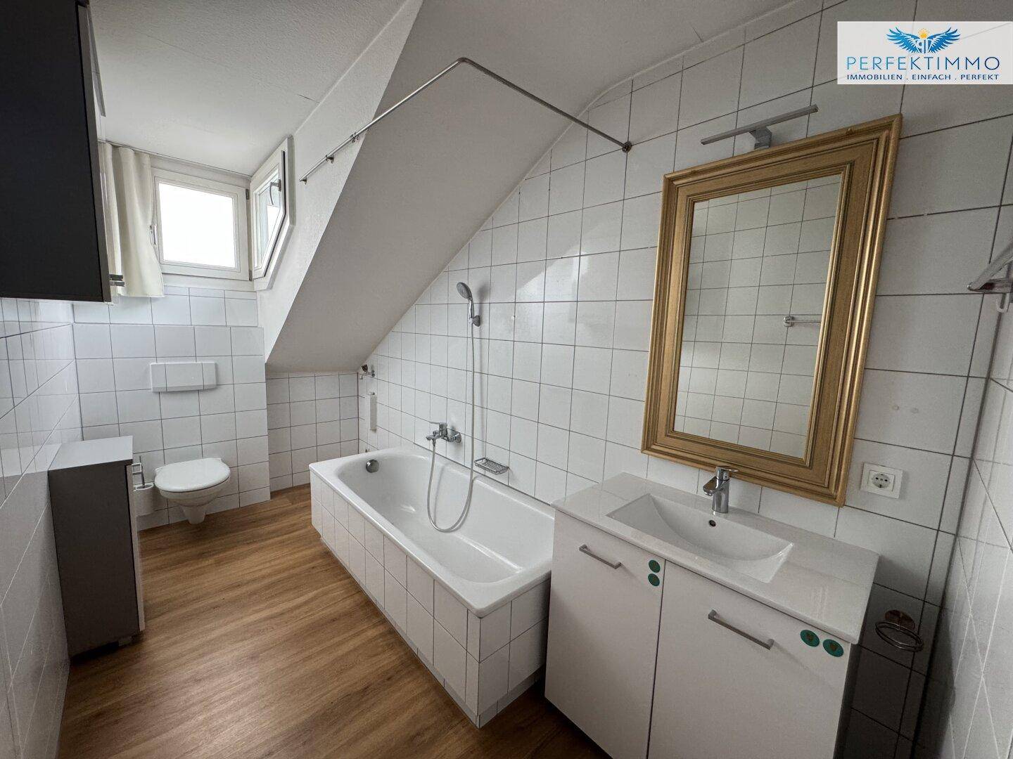 Badezimmer mit Badewanne, WC, Waschbecken und weißen Fliesen unter Dachschräge.