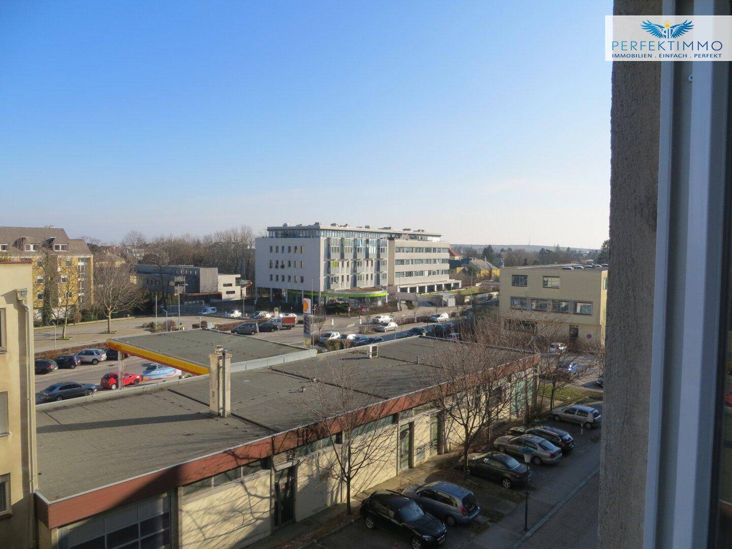 Blick aus dem Fenster auf die städtische Umgebung mit Gebäuden und Parkplätzen.