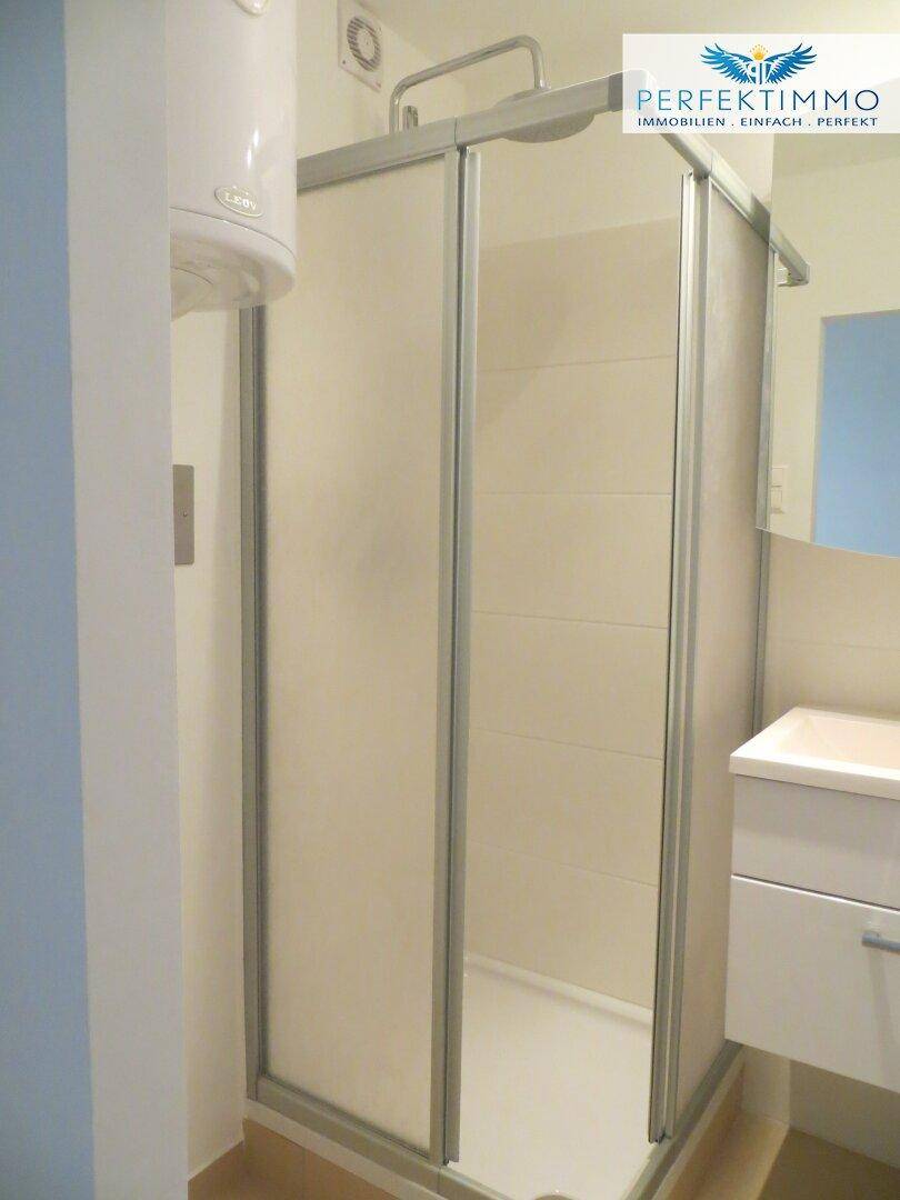 Funktionales Badezimmer mit Duschkabine, Waschbecken und Warmwasserboiler.