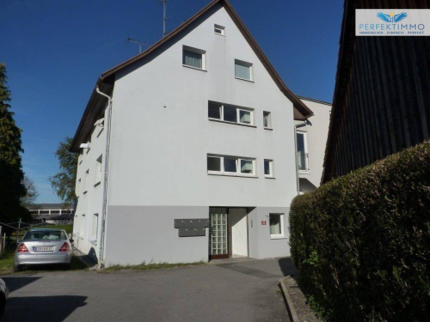 Mehrstöckiges Wohngebäude mit weißer Fassade und einem gepflegten Vorgartenbereich.