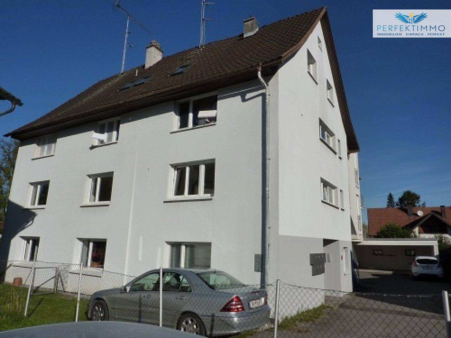 Ansicht des Wohngebäudes von der Seite mit Parkplatz und umzäuntem Bereich.